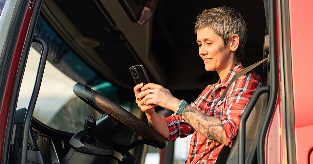 female-trucker-cab-looking-at-phone-1200x628